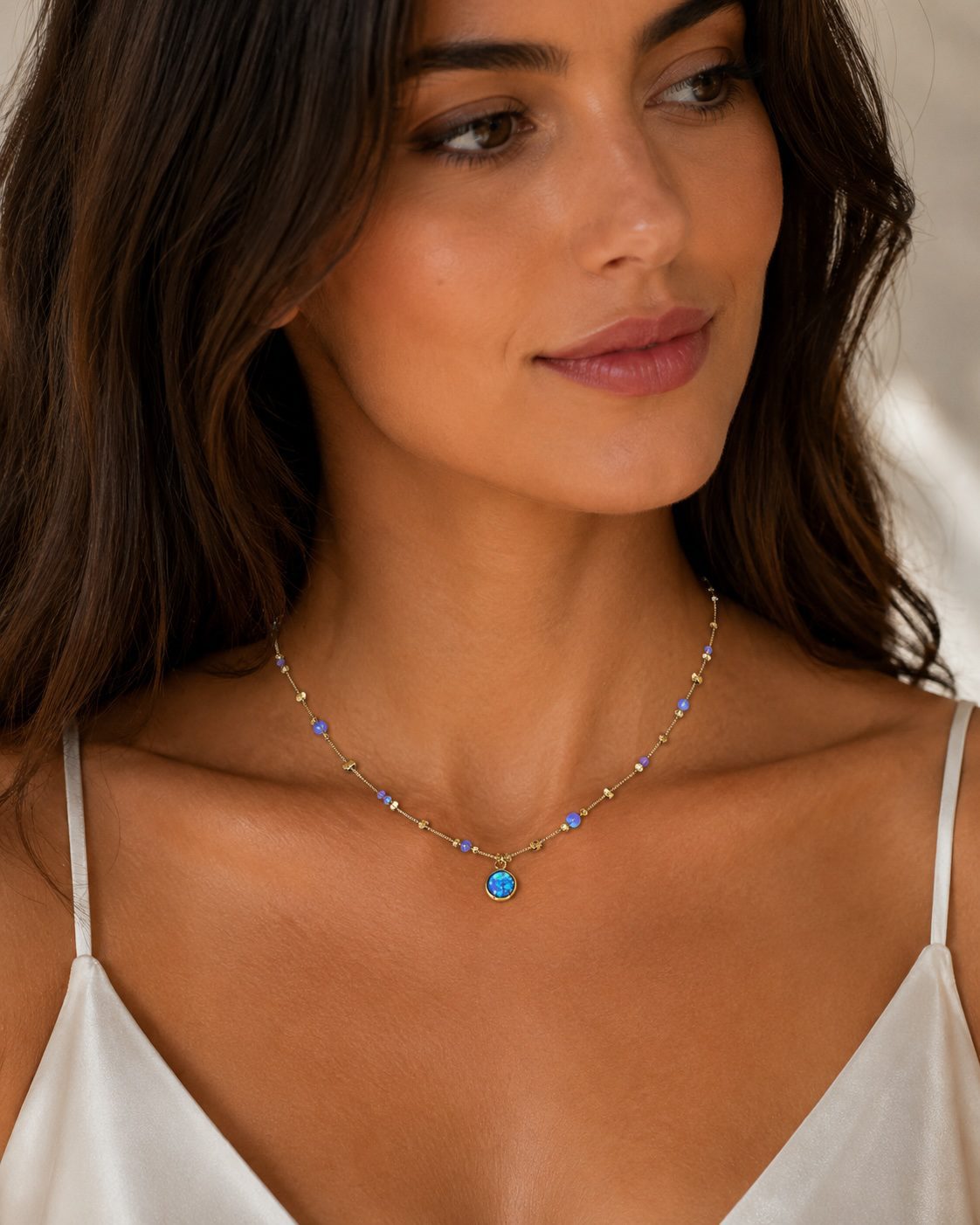 Female model wearing a delicate gold opal necklace with luminous blue opalite gemstones